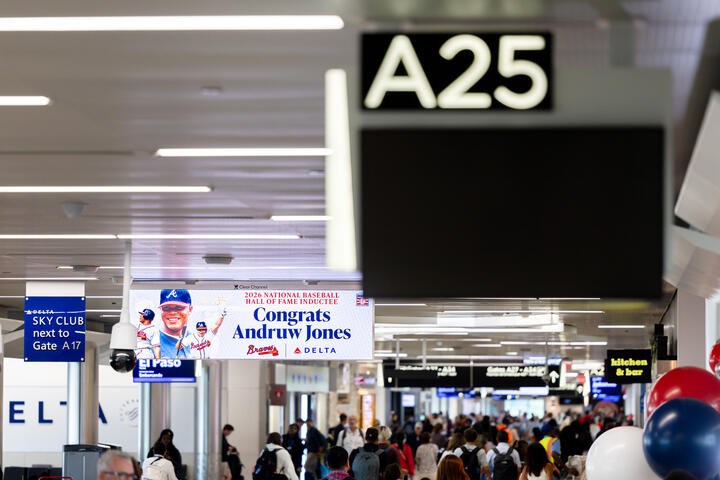Crowded airport concourse near Gate A25, with a digital sign congratulating Andruw Jones on his National Baseball Hall of Fame induction and Delta branding visible throughout the terminal.