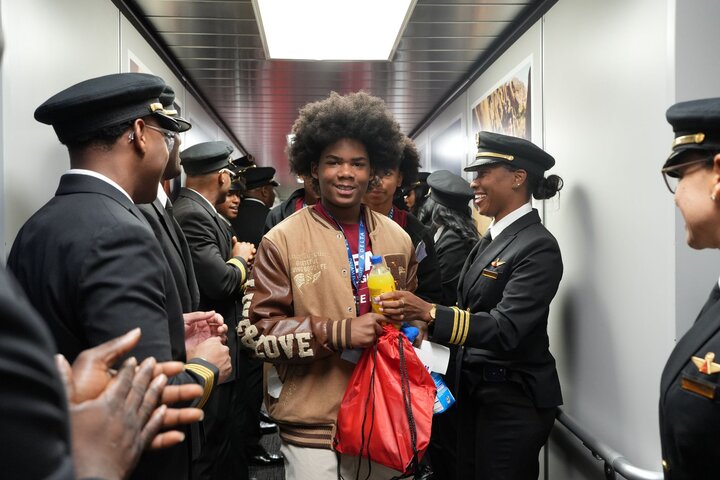 Student participating in Delta’s DREAM Flight walks through a jet bridge lined with Delta pilots welcoming participants before departure.
