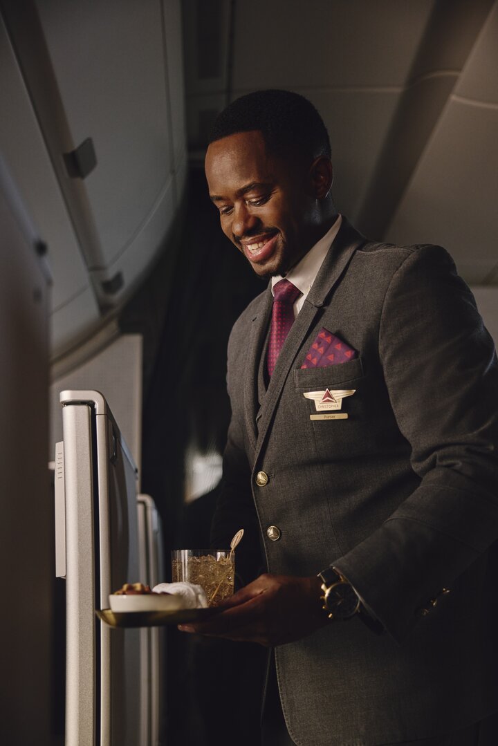 Flight attendant presents a welcome drink and snack service in the Delta One cabin.