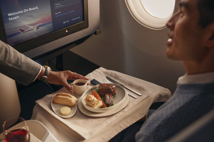 Flight attendant serves a plated meal with bread and vegetables to a passenger in a Delta One cabin.