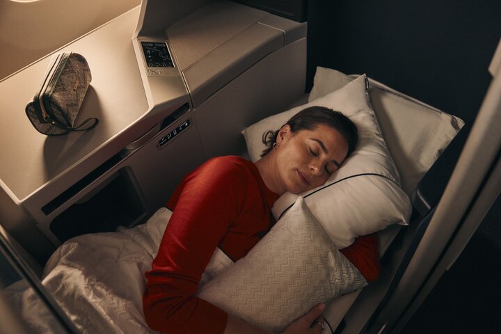 Customer resting in a lie-flat Delta One suite with bedding and pillow.