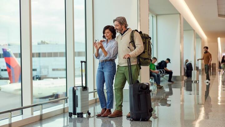 Couple standing next to a window in the airport with a Delta plane tail in the background.