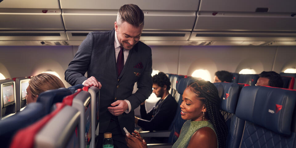 A Delta Flight Attendant assists a customer seated in Delta Comfort+ with their mobile device.