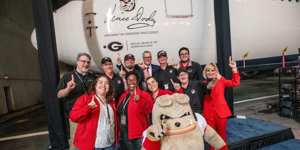Delta leaders and UGA alum stand in front of a Boeing 767-400 featuring a memorial seal honoring renowned UGA football couch Vince Dooley.