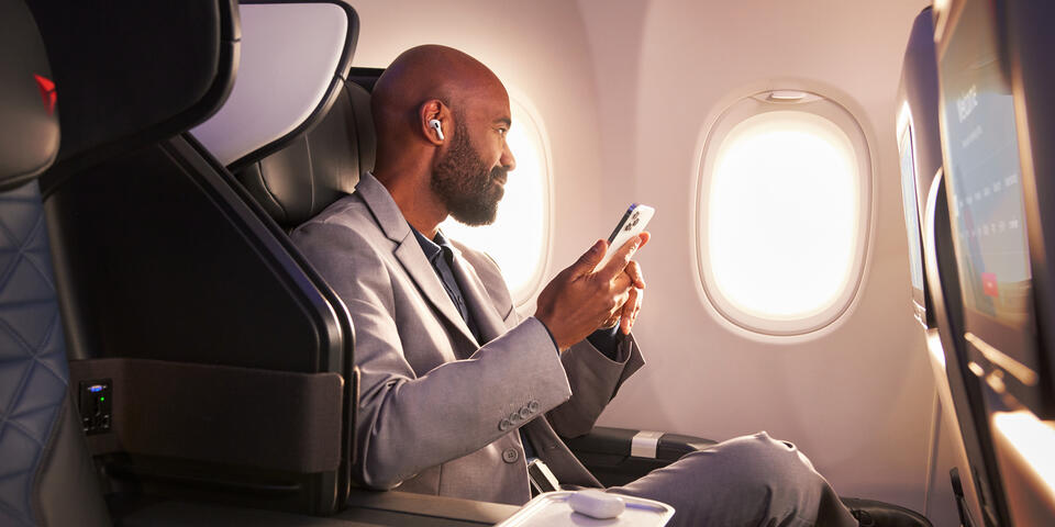 A Delta customer sits in Delta's First Class cabin, holding their phone.