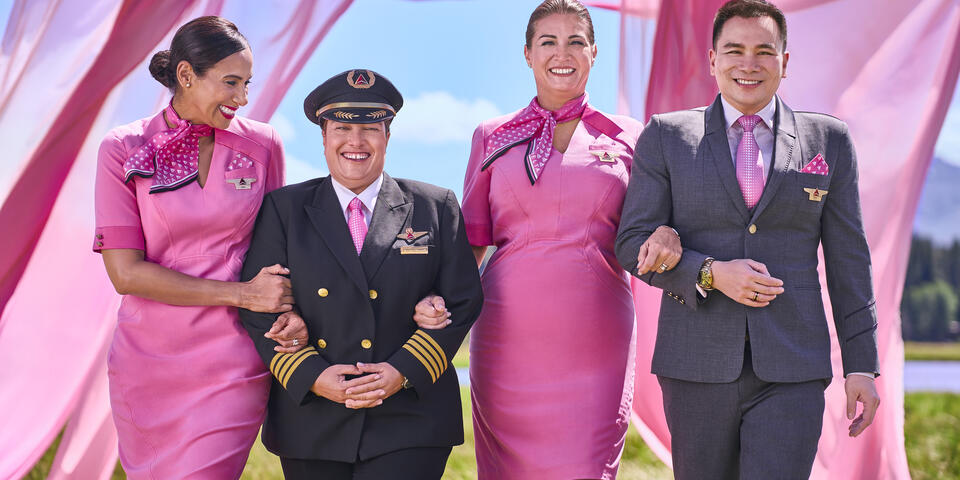 Four Delta employees in pink uniforms walking arm in arm