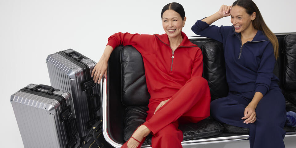 Two smiling women, sitting next to each other dressed in red and navy Spanx outfits.