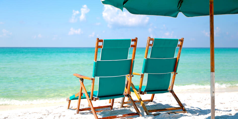 Two empty beach chairs in the sand facing turquoise blue ocean.