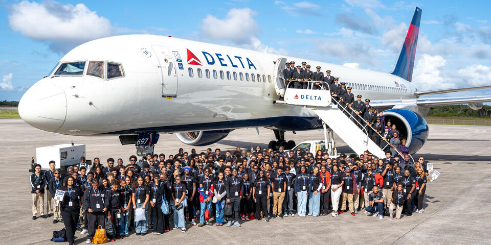 Group shot of DREAM flight attendees standing in front of Delta plane on tarmac. 