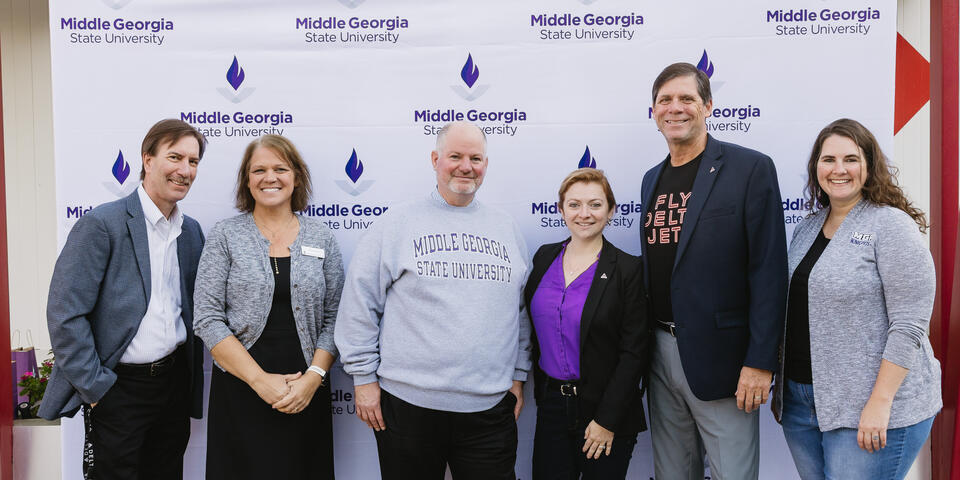 Six people standing in front of a Middle Georgia State University step-and-repeat banner, posing for a group photo.