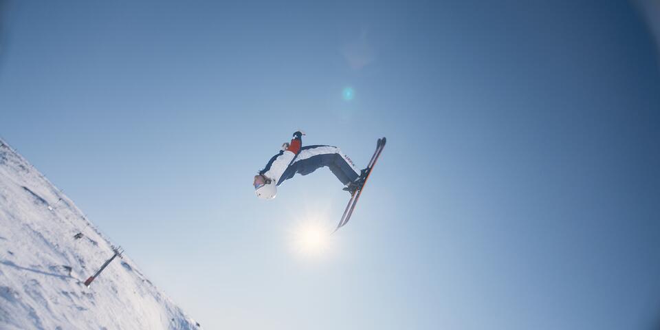 A skier performs a high aerial trick against a clear blue sky on a snowy mountain slope