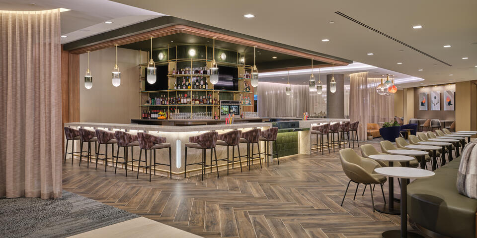 Lounge bar with high‑back stools, illuminated shelving, warm lighting and adjacent seating areas with small tables