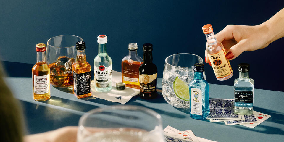 A lineup of airplane bottles of alcohol against a blue background