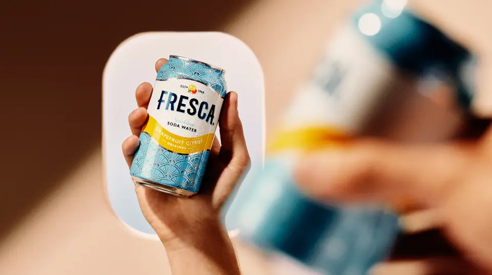 Hand holding a chilled Fresca grapefruit citrus soda can, with an airplane window softly blurred in the background.