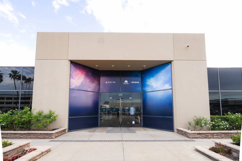 Exterior entrance of a building featuring Delta and Paramount+ Star Trek 60 branding, with colorful space-themed graphics surrounding glass doors.