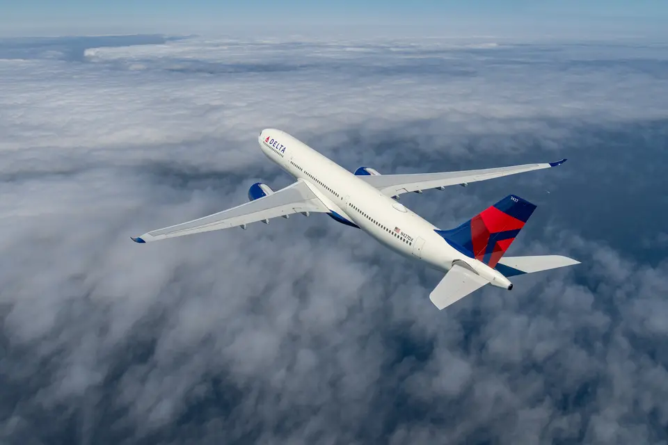 A Delta Air Lines A330-900 flies over clouds.