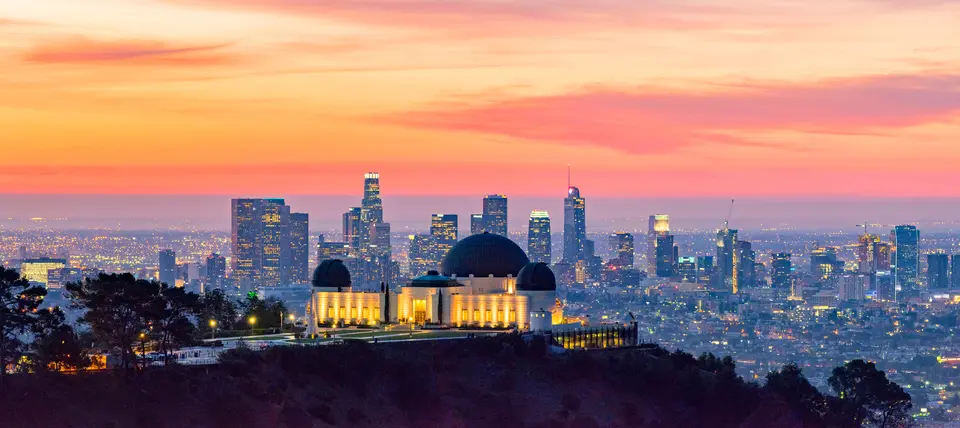 Los Angeles skyline at dawn with Griffith Park Observatory in the foreground.