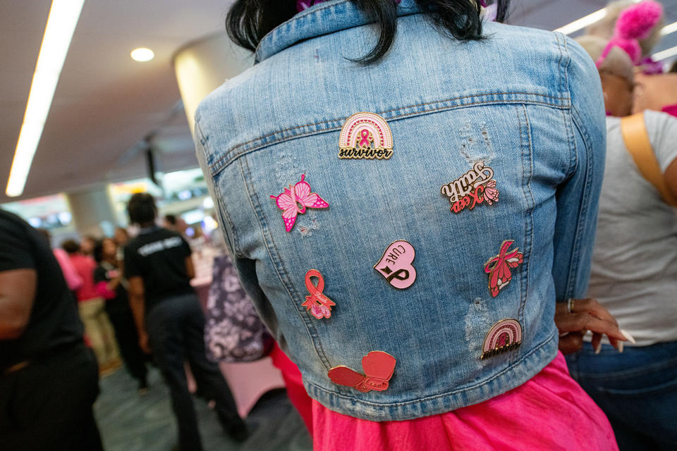 A breast cancer survivor shows off her collection of Breast Cancer Awareness pins on the back of her jean jacket.