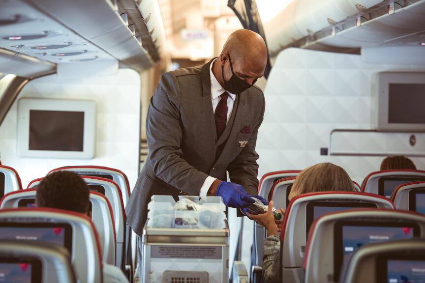 A masked flight attendant serves customers.