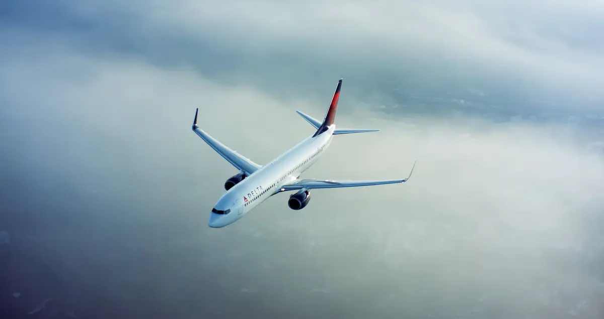 A 737-900 flies through clouds with a cityscape underneath.