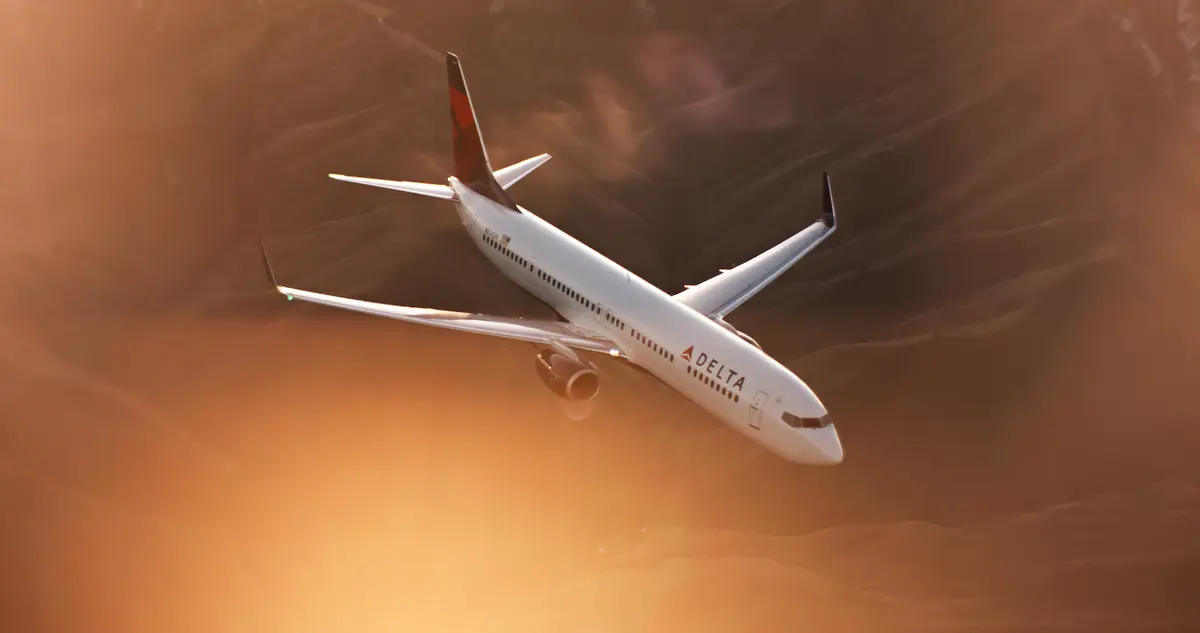 A 737-900 flies while a mountainous terrain displays in the distance.