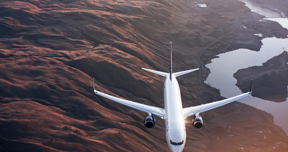 A 737-900 flies over mountains and a river.