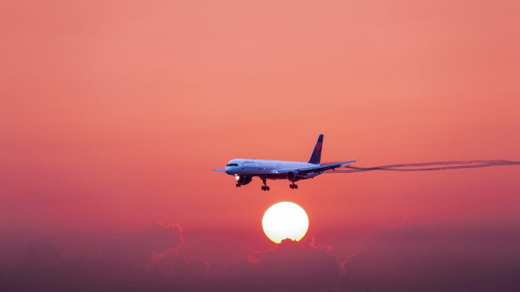 A 757-300 in flight with a red-hued sunset and cloud background.