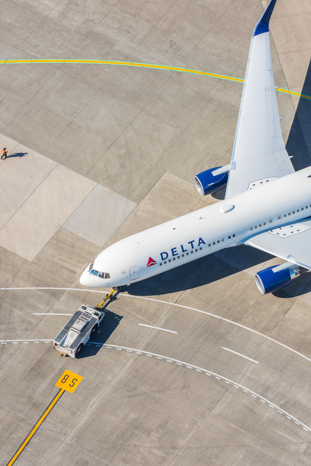 A 767-300 on the runway complemented by various objects in the background (boundary lines on the runway & a below wing employee).