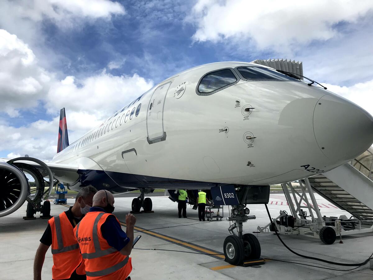 A220-300 parked on tarmac with stair truck and employees