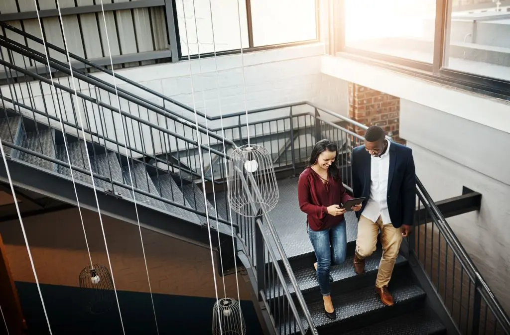 Two people walking down a flight of stairs looking at a tablet.