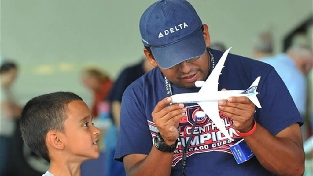 Man holds model airplane while boy looks on.