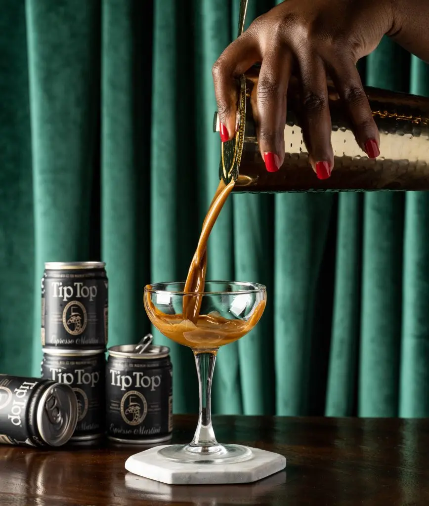 A hand pouring Tip Top Proper Cocktails' Espresso Martini into a martini glass.