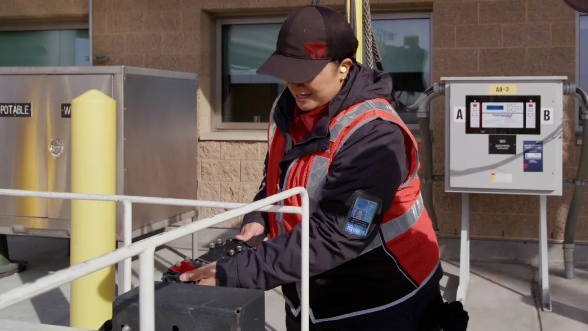 Delta Ramp Agent Sinai Pauni (left) plugs in an electric bag tractor for charging at Salt Lake City International Airport (SLC).