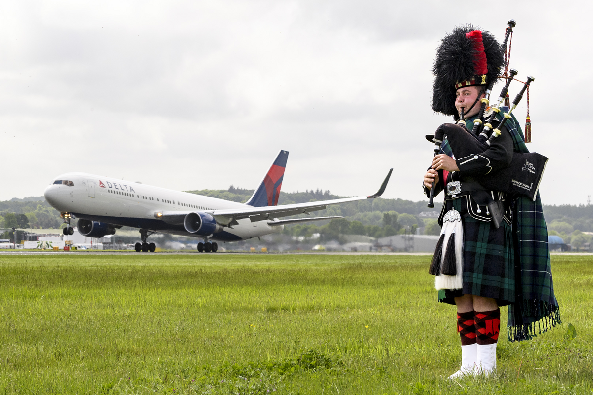 A bagpiper plays in front of a Delta aircraft at the Edinburgh Airport.