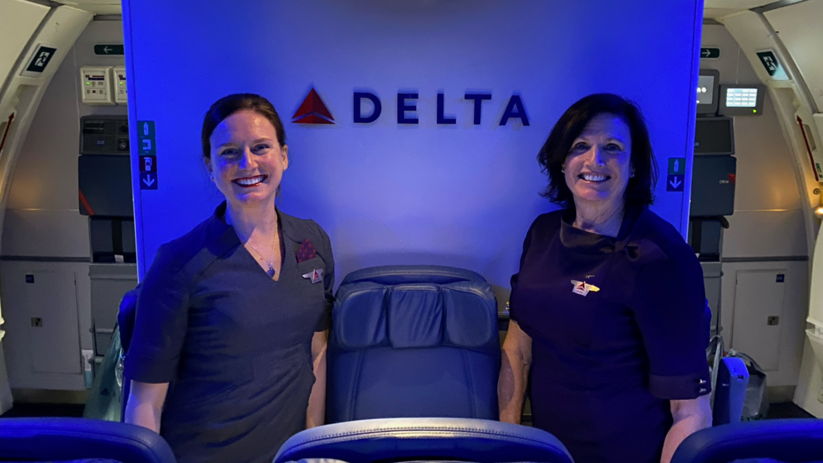 A mother and daughter duo who have nearly 30 years of combined service at Delta pose for a photo onboard a plane.