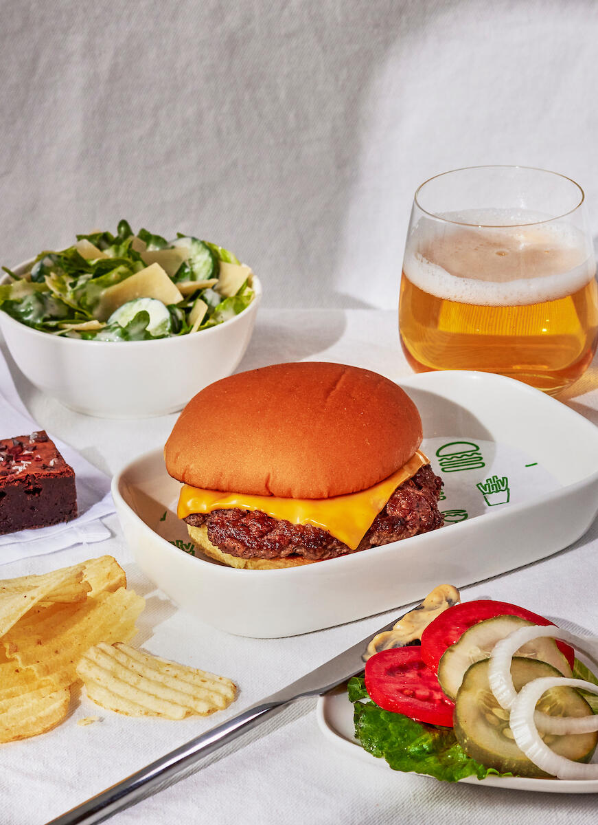 A Shake Shack burger with a side of chips, a salad, and burger fixings.