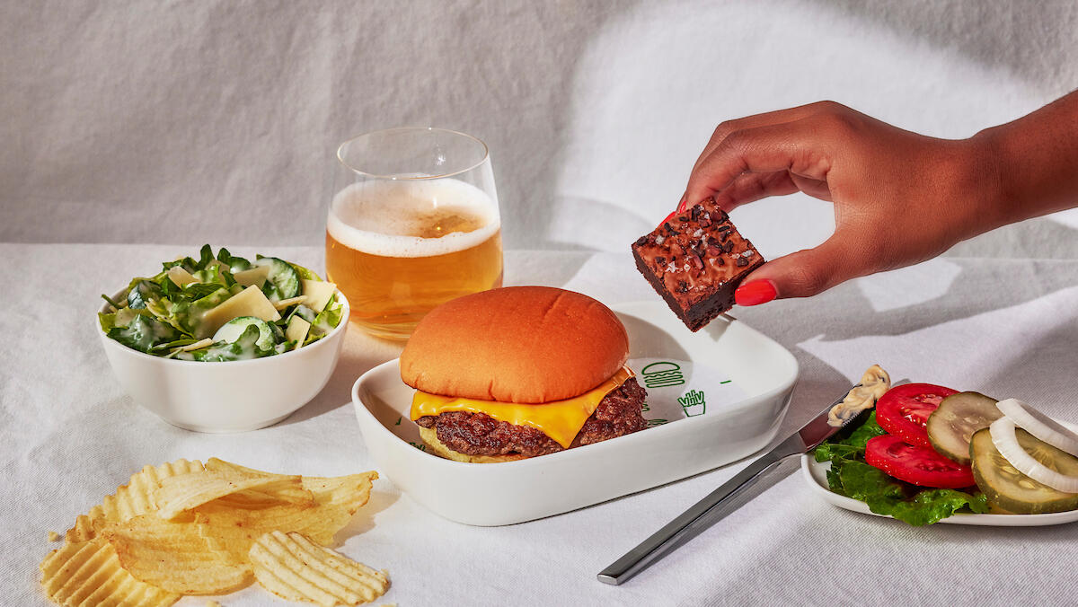 A Shake Shack burger with a side of chips, a salad, and burger fixings.