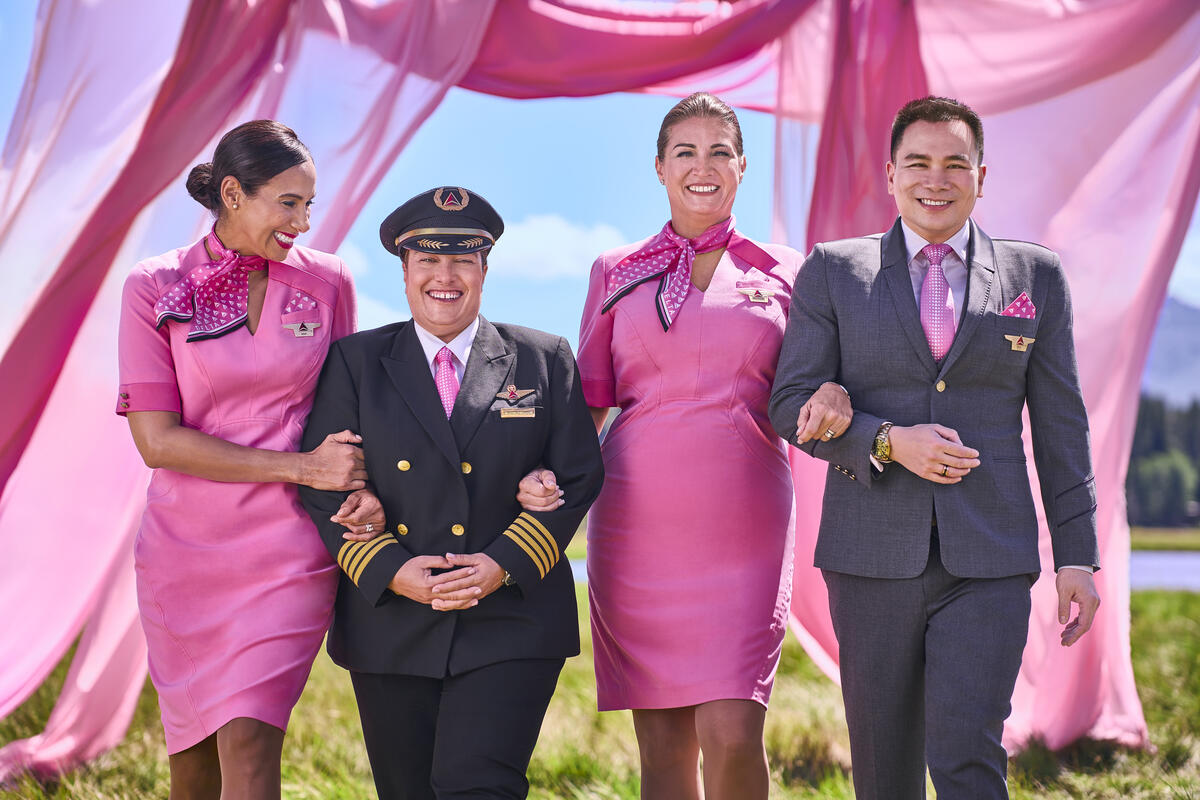 Four Delta employees in pink uniforms walking arm in arm