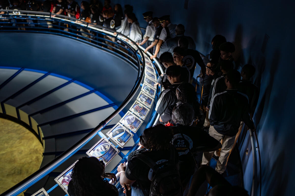 DREAM flight participants walking along a curved ramp lined with astronaut photos and memorabilia in a space-themed exhibit.