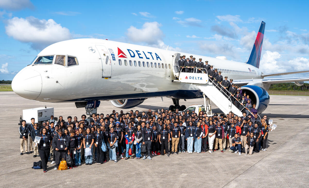 Group shot of DREAM flight attendees standing in front of Delta plane on tarmac. 