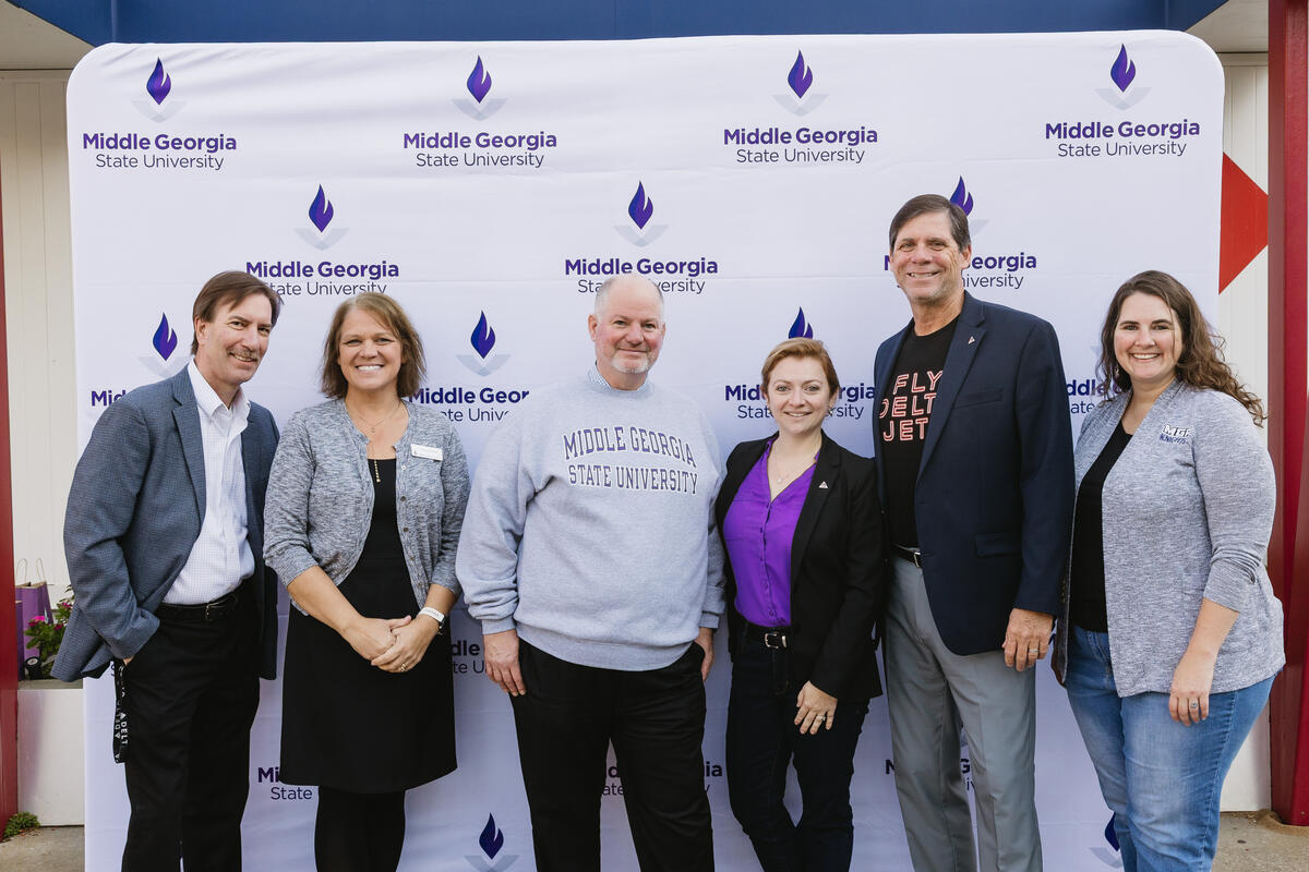 Six people standing in front of a Middle Georgia State University step-and-repeat banner, posing for a group photo.