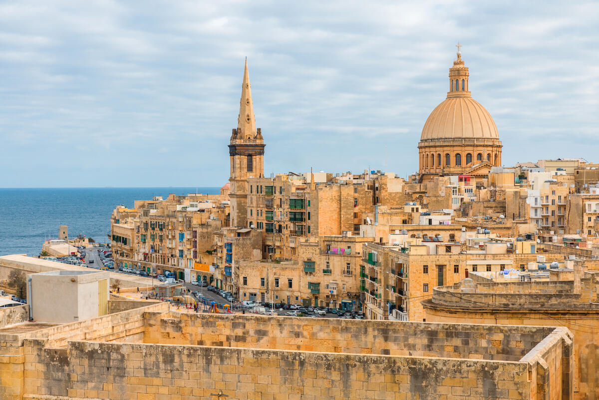 Historic limestone city with a large domed church and spire overlooking the sea.
