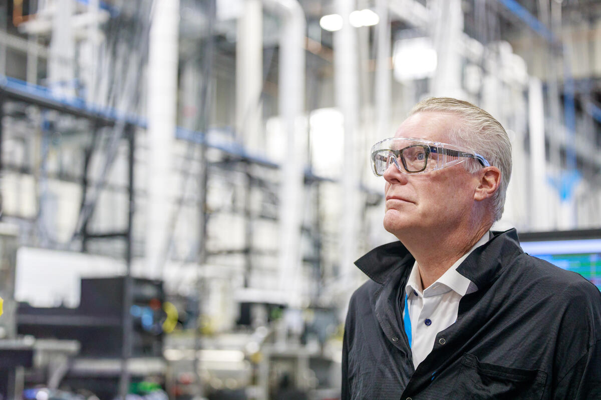 Ed Bastian wearing safety glasses standing inside an industrial facility with machinery and pipes in the background.