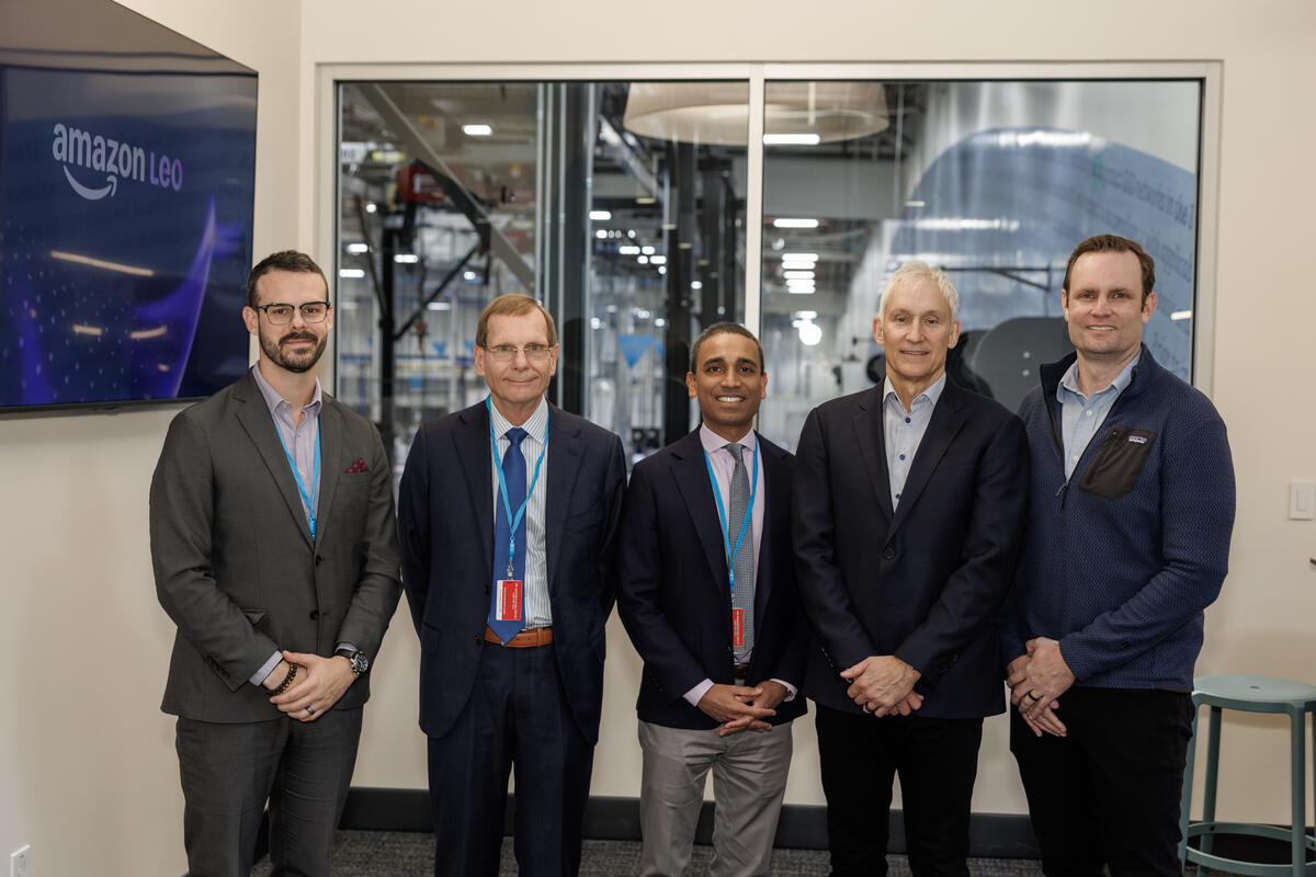 Members of Delta and Amazon Leo teams pose for a picture with factory as backdrop.
