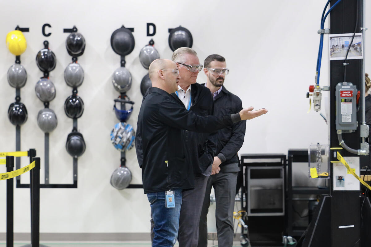 Three people wearing safety glasses review equipment inside an industrial facility.