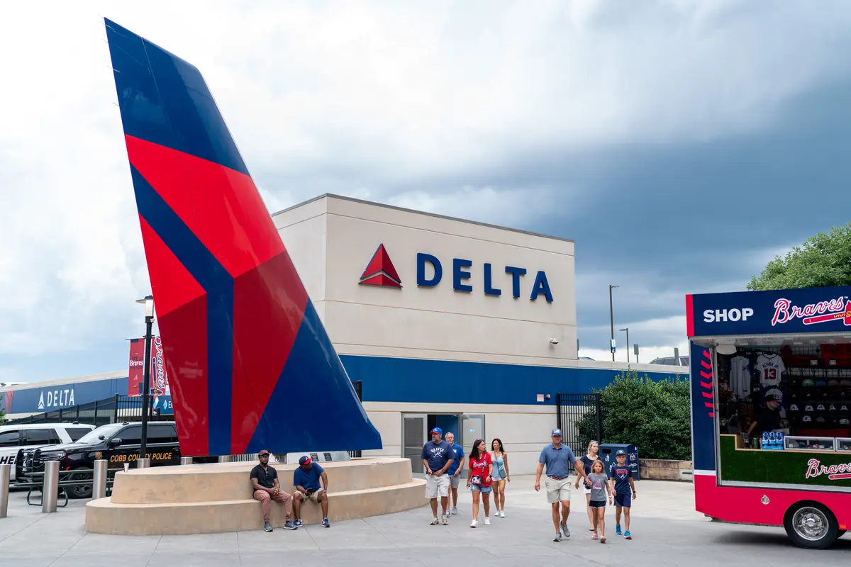 People walk outside a stadium concourse near a large Delta airplane tail sculpture and a Delta-branded building, with a Braves merchandise shop nearby.