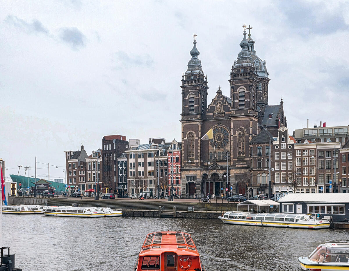 Historic waterfront church in Amsterdam with canal boats in the foreground.