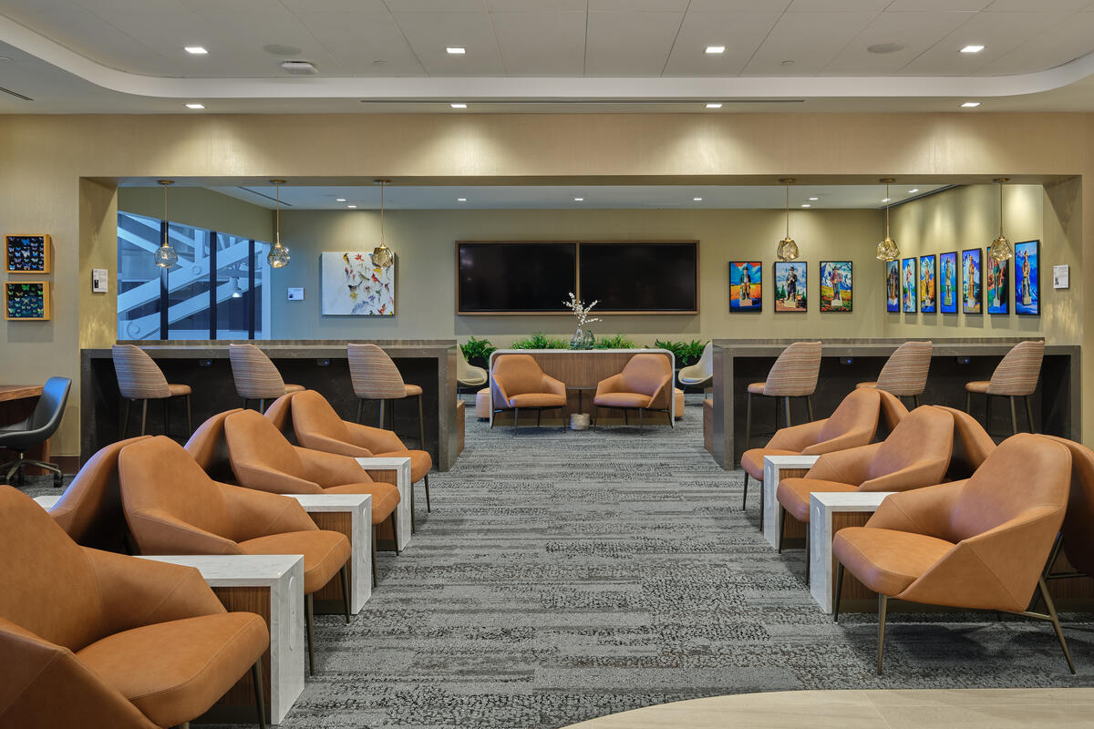 North lounge area with rows of tan lounge chairs, bar‑height seating, modern lighting and colorful artwork on the walls