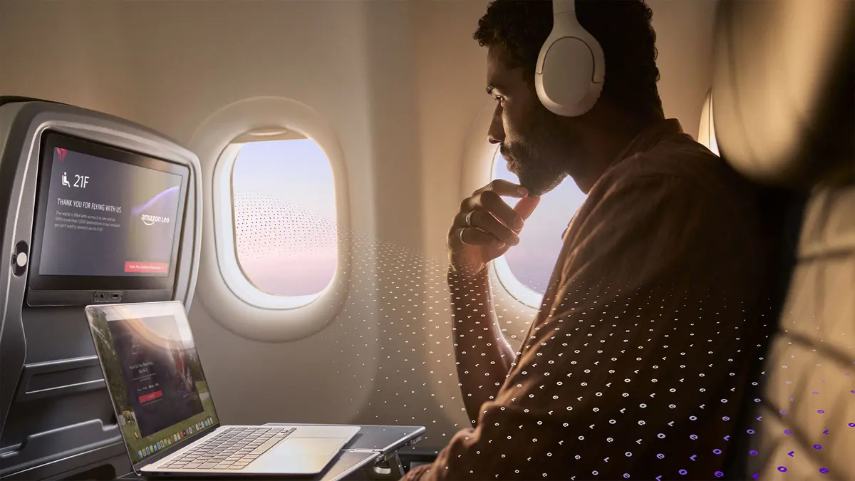 A passenger seated by an airplane window uses a laptop and wears over‑ear headphones, with an in‑flight entertainment screen visible and a subtle digital pattern overlay.