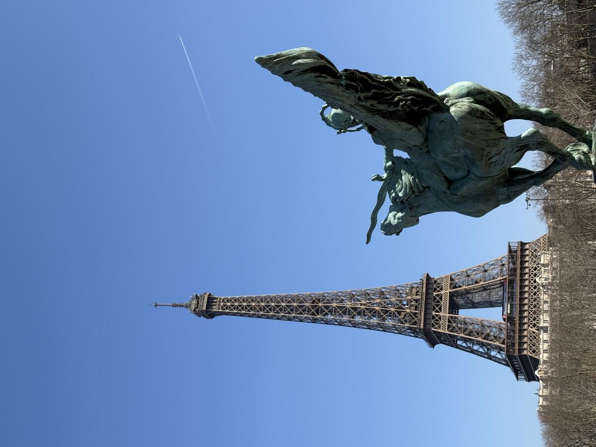 A bronze statue of the winged horse Pegasus is in the foreground, with the Eiffel Tower prominent in the background under a blue sky, viewed from the Pont de Bir-Hakeim.